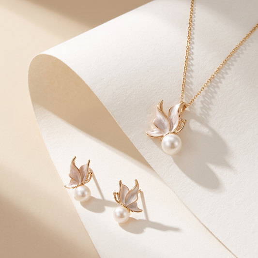 A gold-tone jewelry set featuring a necklace and matching stud earrings with leaf-shaped pearly enamel details and small pearl-like beads, displayed on a curved cream surface.