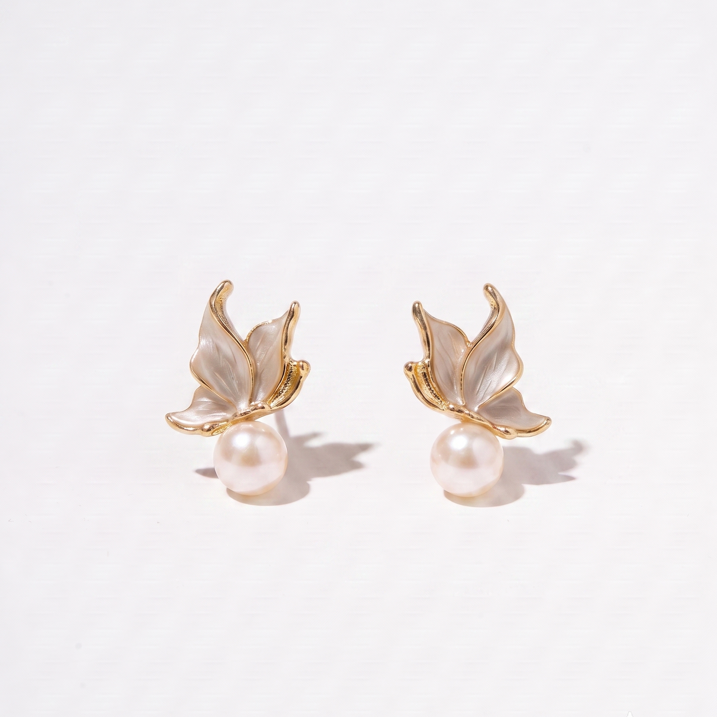 A pair of gold butterfly stud earrings with iridescent white mother-of-pearl wings and a single pearl hanging below each butterfly, photographed on a clean white background.