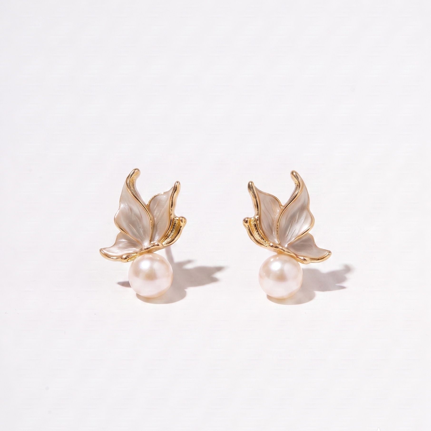 A pair of gold butterfly stud earrings with iridescent white mother-of-pearl wings and a single pearl hanging below each butterfly, photographed on a clean white background.