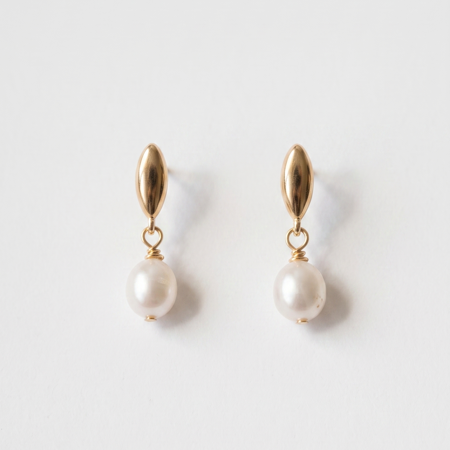A pair of gold drop earrings with a small teardrop-shaped gold top and a dangling white pearl, shown on a clean white background.