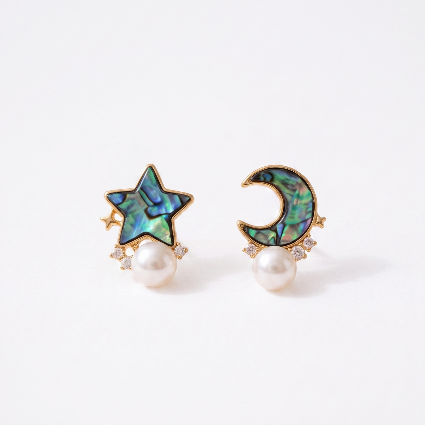 A pair of gold-toned stud earrings featuring an iridescent abalone shell star and crescent moon design, each hanging from a white pearl, set against a clean white background.