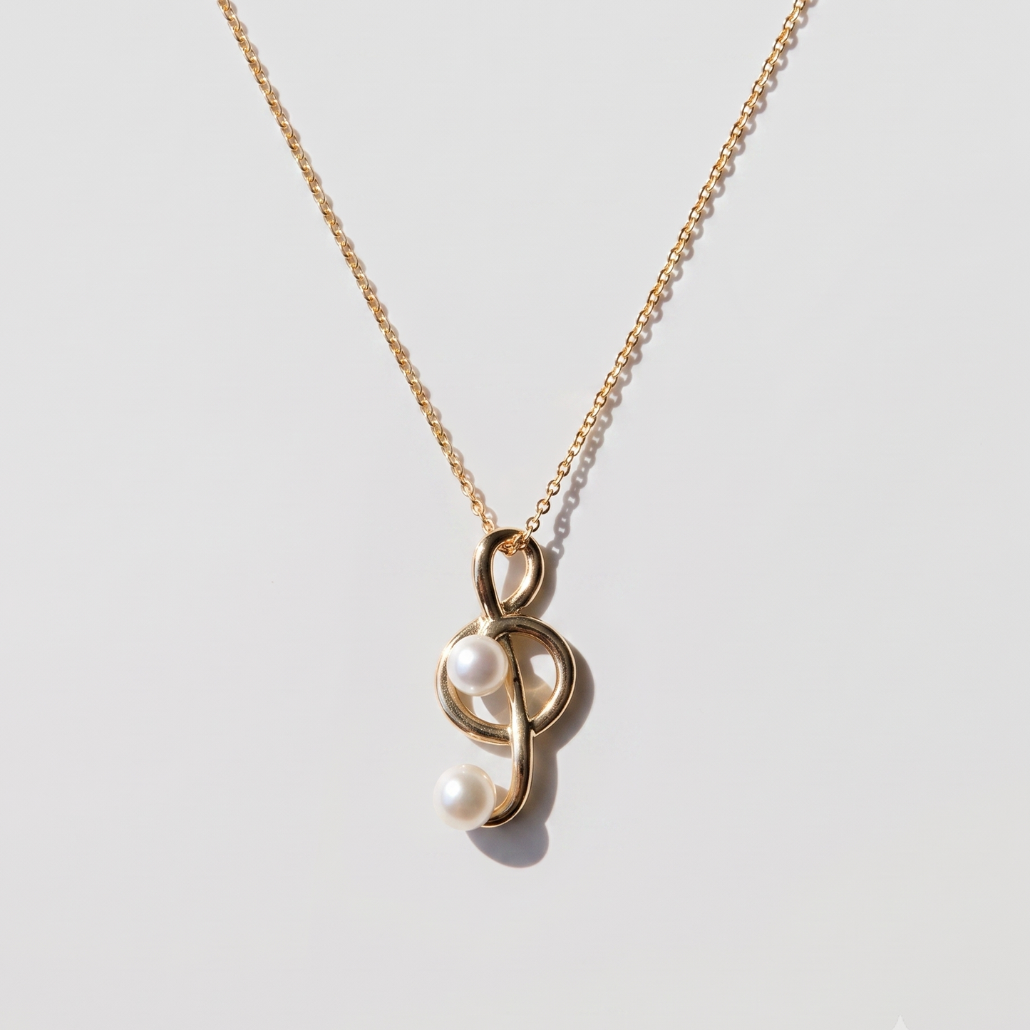 A delicate gold chain necklace featuring a unique pendant with two white pearls nestled inside a polished gold loop, displayed on a clean light gray background.