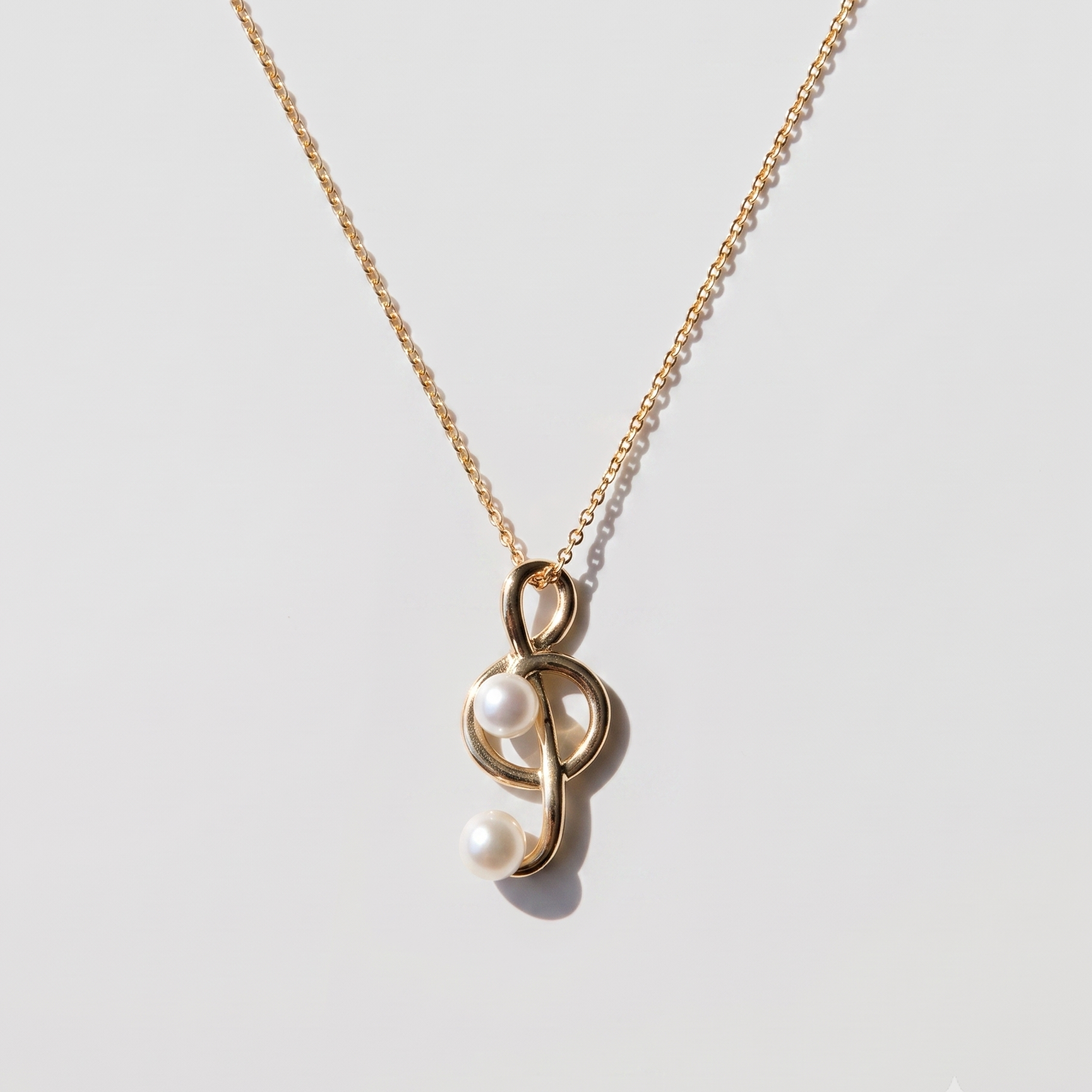 A delicate gold chain necklace featuring a unique pendant with two white pearls nestled inside a polished gold loop, displayed on a clean light gray background.