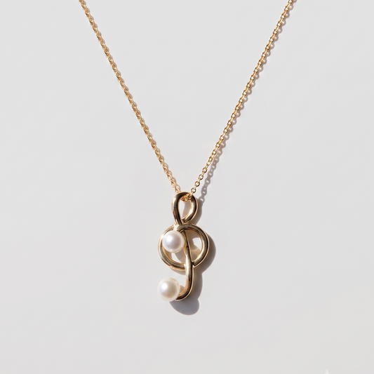 A delicate gold chain necklace featuring a unique pendant with two white pearls nestled inside a polished gold loop, displayed on a clean light gray background.