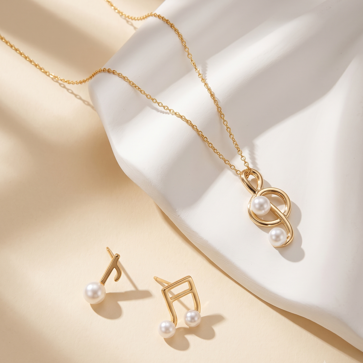Gold necklace and matching stud earrings with pearl accents, arranged on a white sculptural display against a warm beige background with soft shadows.