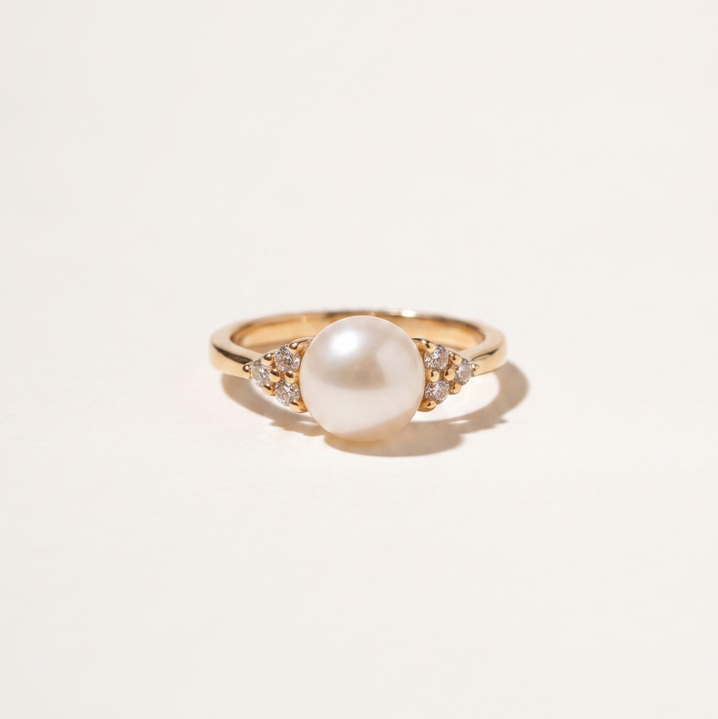 A gold ring featuring a large white pearl center stone and small clear accent stones on either side of the band, photographed on a clean off-white background.