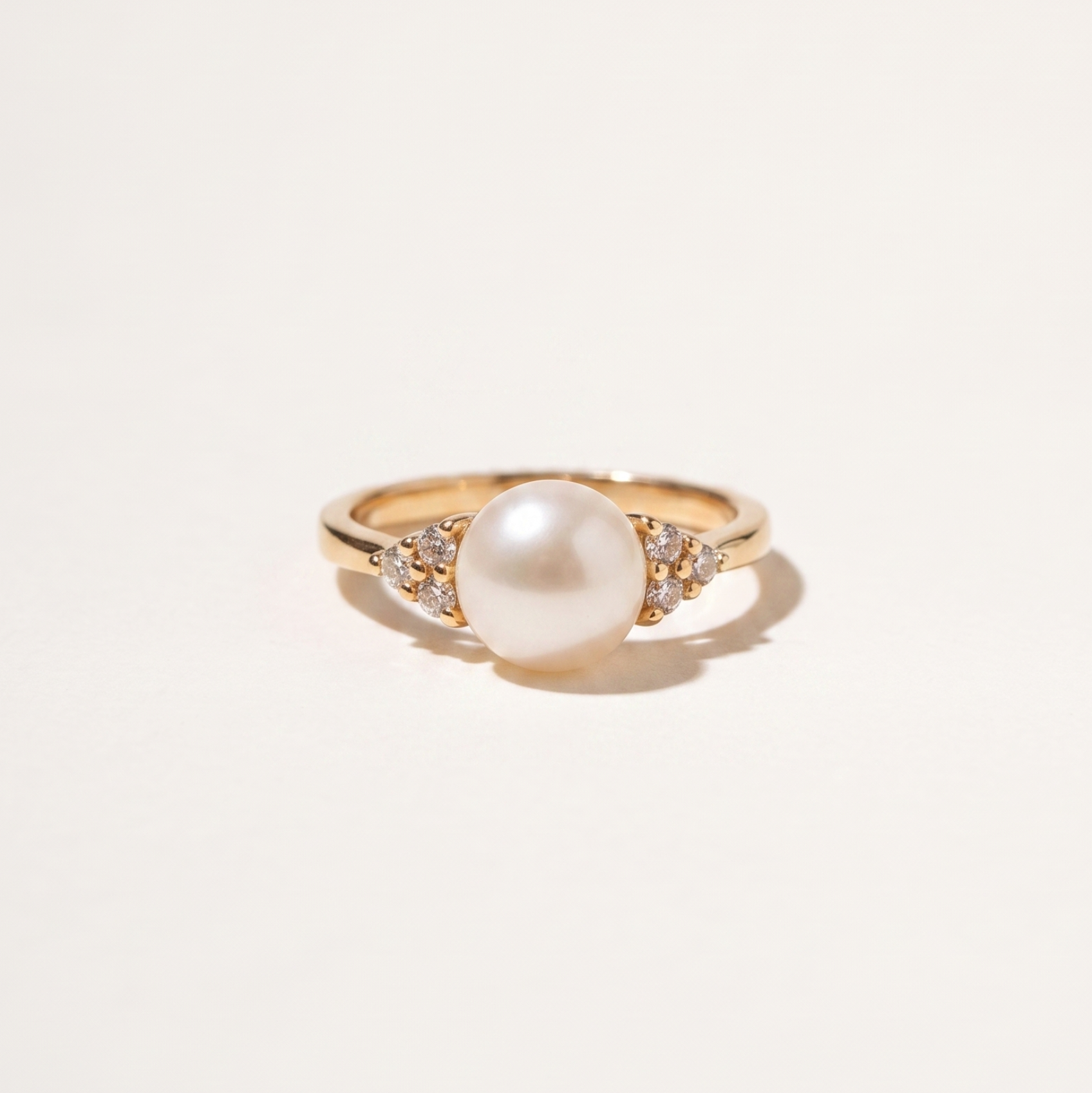 A gold ring featuring a large white pearl center stone and small clear accent stones on either side of the band, photographed on a clean off-white background.