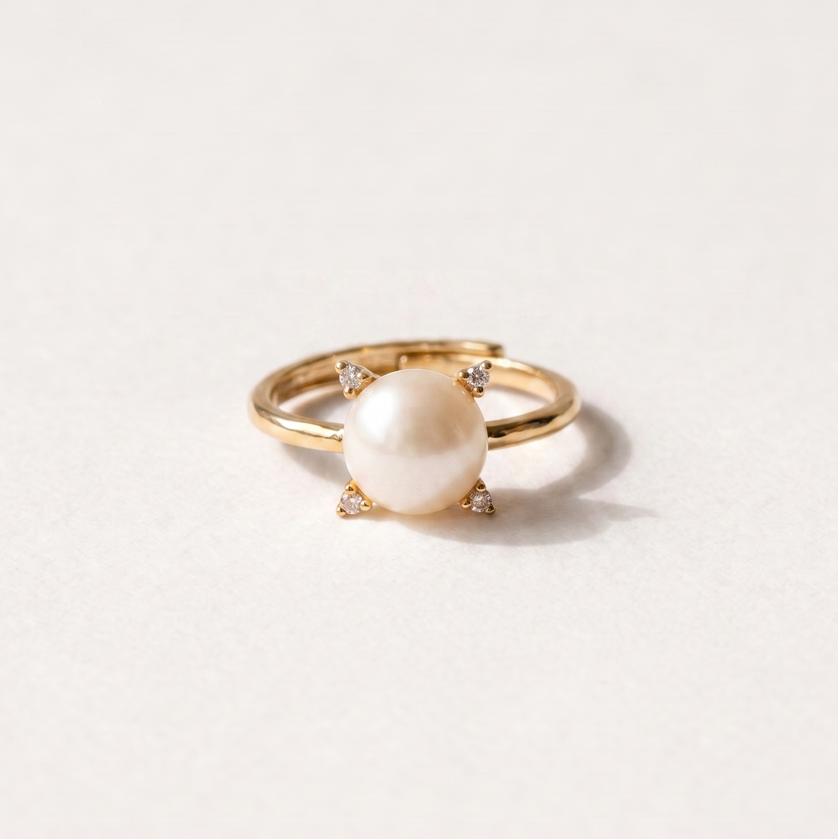 A gold ring featuring a round white pearl held in a four-prong setting with tiny accent stones, photographed on a clean white background.