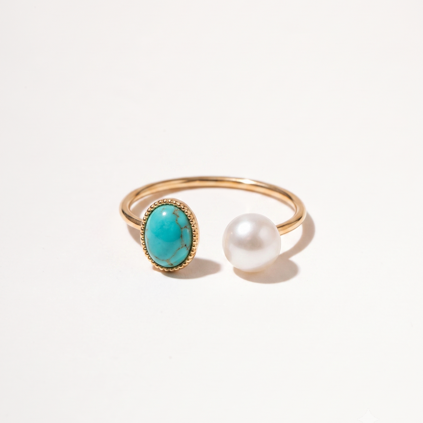 A gold open-band ring featuring an oval turquoise stone and a single white pearl, photographed on a clean white background.