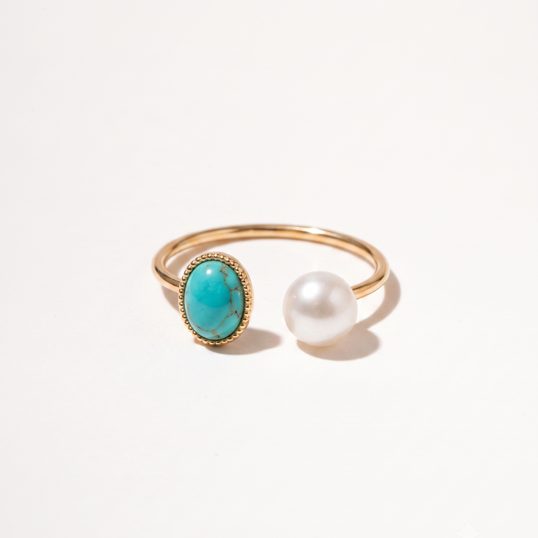A gold open-band ring featuring an oval turquoise stone and a single white pearl, photographed on a clean white background.