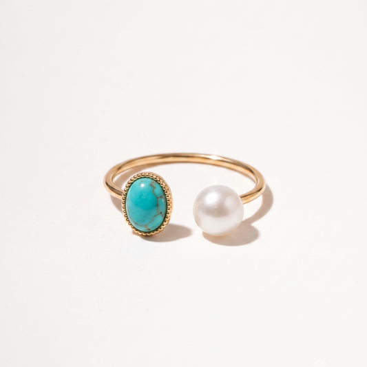 A gold open-band ring featuring an oval turquoise stone and a single white pearl, photographed on a clean white background.